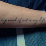 A photo of a script tattoo on the forearm, reading "My Work of Art is My LIfe" before any treatments.