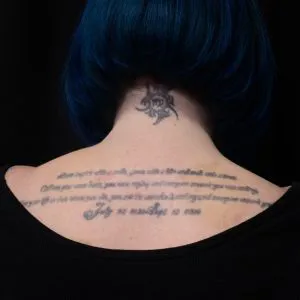 A photo of the script tattoo on the back shoulders, before any laser tattoo removal treatments.